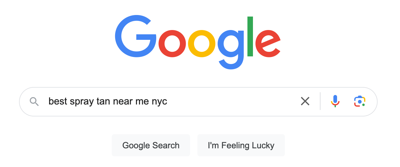Image of a Google search page with the query "best spray tanning near me" typed into the search bar. Below the search bar, there are two buttons labeled "Google Search" and "I'm Feeling Lucky"